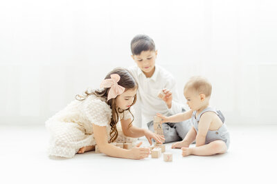 A photo of 3 young siblings playing with wooden blocks at a photography studio in Fort Worth TX.