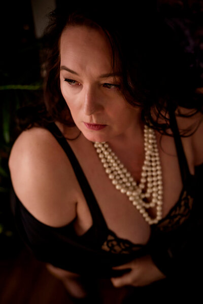 Close up of a Mature woman wearing many strands of pearls and black bra for her photoshoot at the pouting room