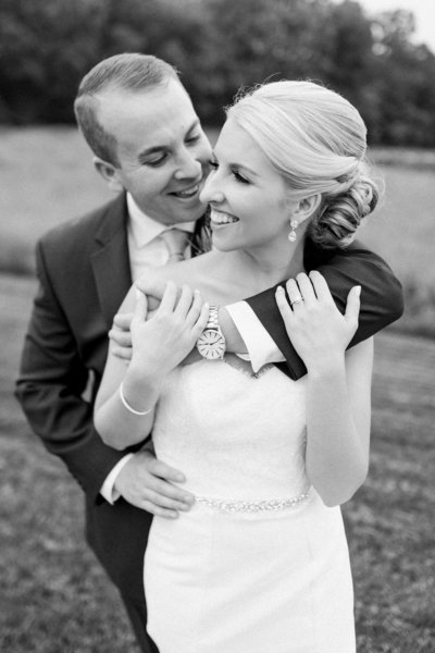 groom embraces his bride with his arms wrapped around her as she smiles off to the side