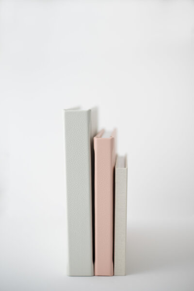 Wedding photo albums in gray, pink, and cream stacked together