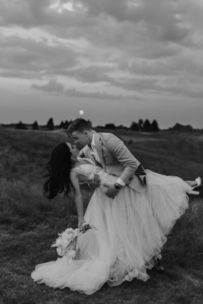 black and white bride and groom dip kiss under the full moon