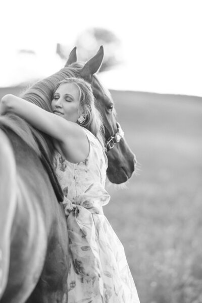A blonde woman in a long dress hugs her sorrel barrel horse's neck while posing for a black and white horse portrait for Oklahoma Horse Photographer Rachel Griffin