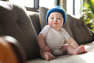 Baby boy sitting on couch making kiss face for a Minneapolis family photographer