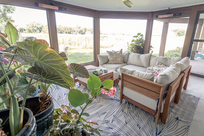 Inside a screened-in porch with cozy furniture, plants, and ceiling-mounted heaters. 