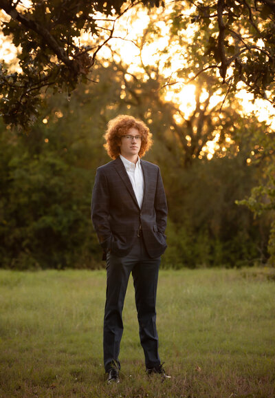 senior-boy-with-red-afro-in-suit-standing-with-hands-in-pockets-in-arlington-tx-park