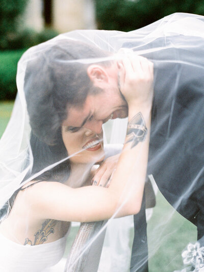 Film Santa Barbara elopement and wedding photograph of a laughing bride with tattoo holds her laughing groom from under the bridal veil.