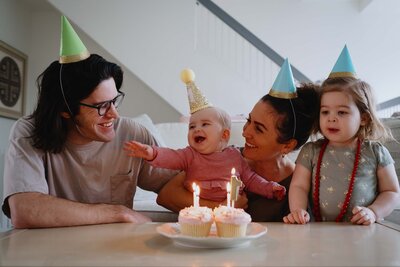 Mom, dad, and toddler celebrate their baby's first birthday with cupcakes and party hats, taken during a Los Angeles Family photography session.