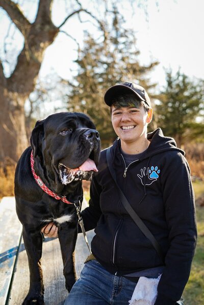 Woman in black hoodie and Cane Corso smile at camera.