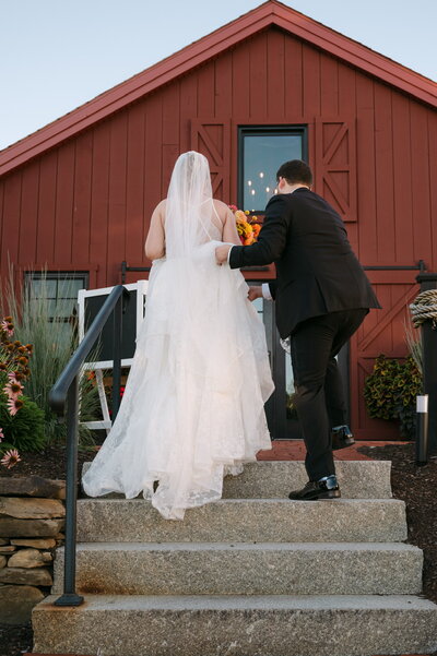 Bride and groom walking up the steps of a rustic red barn during their New England wedding, photographed by Sarah Ferrazzani.