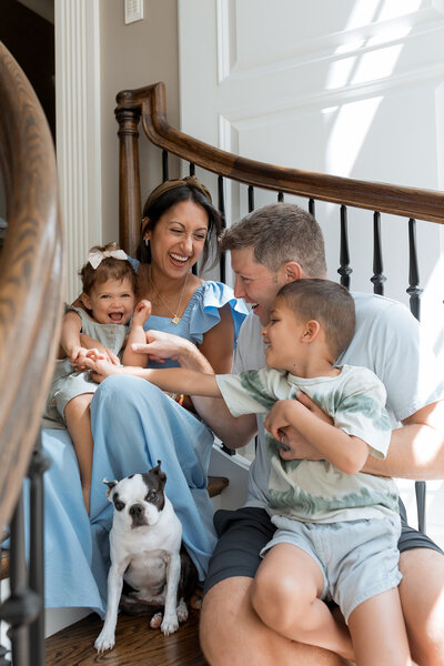 Family Photographer, a young family huddle on the stairs smiling with their french bull dog