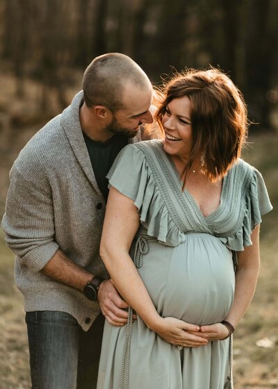 A pregnant woman and her husband standing in the woods for a Pittsburgh maternity photoshoot.