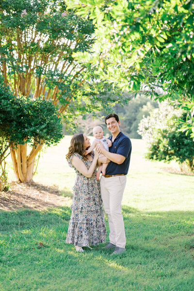 Couple with baby boy smile during Summer photo session in Raleigh NC