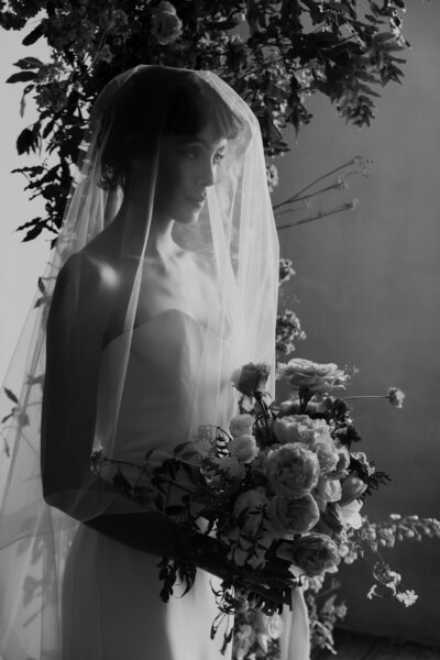 bride holding bouquet with veil over her face