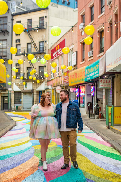 A couple with their arms around each other walking along a colorful street.