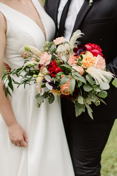 Detail photo of bride and groom holding whimsical greenery and colorful flowers bouquet