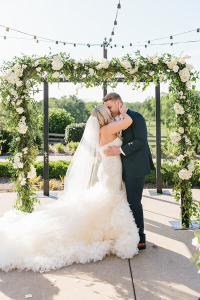 White and Green Flower Arbor with bride and groom kissing after ceremony