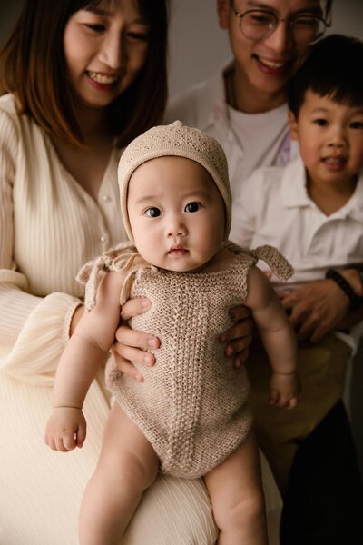 Carinas Family holding her on their knee during their family photoshoot at the studio in new plymouth of aimee kelly photography