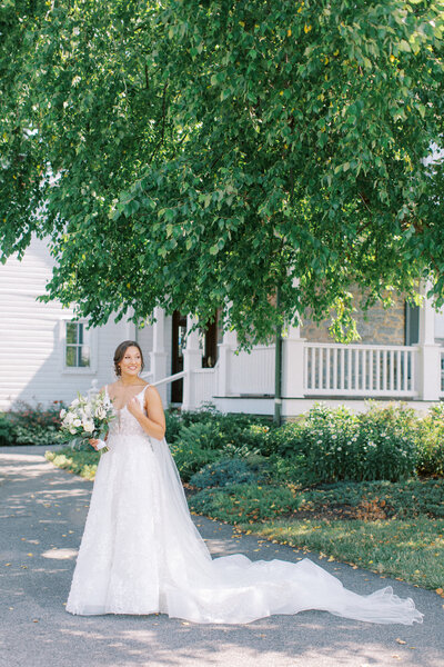 A bride poses in front of a historic mansion and green tree
