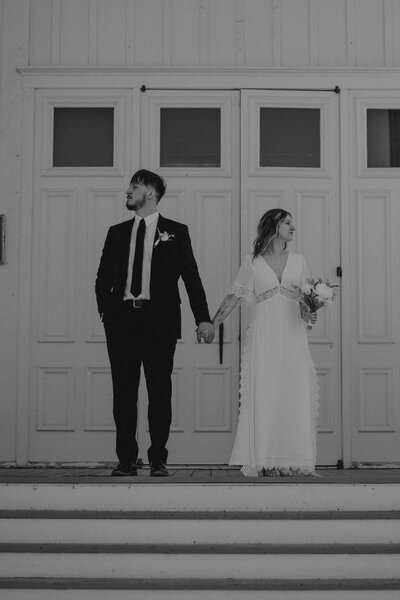A married couple stands in a mysterious, editorial fashion on the steps of a vintage church 