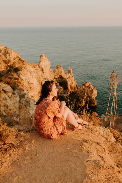 Lisbon wedding photographer exploring the beaches in the Algarve. Orange and teal dress blowing in the breeze on the Portugl coast.