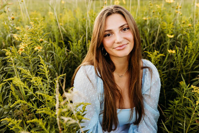 teen girl in a light blue top smiling in a field of goldenrod and captured by Green Bay Senior Photographer Ashley Kalbus