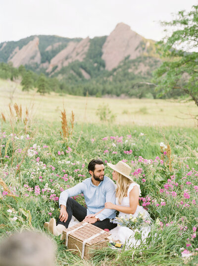 Couple sitting in flowers with mountains behind them during Denver couples photo session