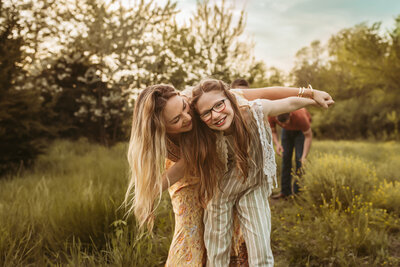 Mom in yellow floral dress plays airplane with her daughter in a blue stripe romper in field at family sunset photo session