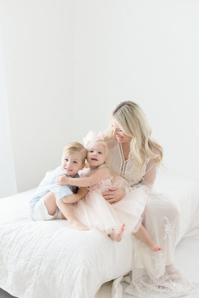 A mom holding on tight to her two young children in all white studio by NJ Family Photographer