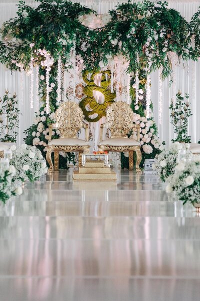 Elegant wedding stage adorned with flowers and greenery, featuring a golden bridal sofa.