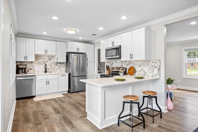 Bright kitchen featuring white cabinets, stainless steel appliances, backsplash, and a center island with bar seating in Wilmington NC. 