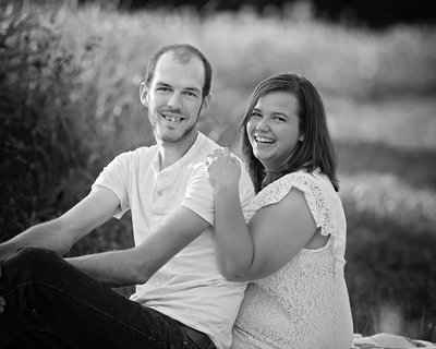 Josh and Jeanette sit in a field laughing at a family session in Greenville Pa.
