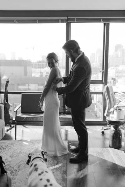 Hudson Valley elopement photographer standing next to the ocean leaning against a knee wall with boats in the background