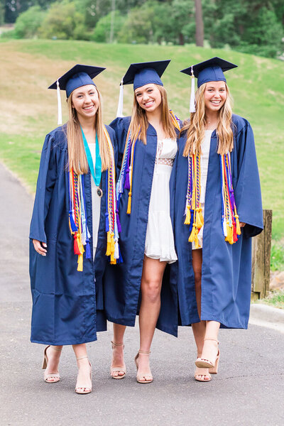 High school senior girls with cap and gown walking in the park in Raleigh, NC.