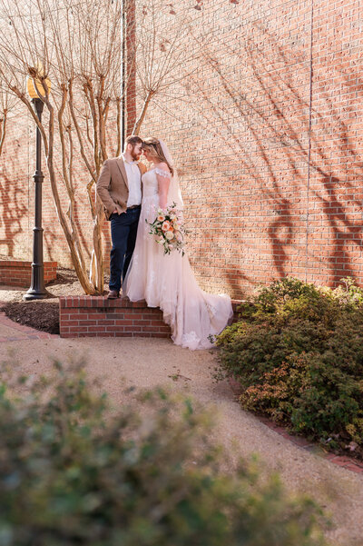 A young blonde couple touching noses after their winter wedding in downtown Oxford at sunset enjoying their Raleigh wedding photography by JoLynn Photography
