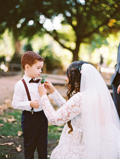 bride puts on a bouttoniere on her ring bearer on her wedding day. it is a bright photo captured on film