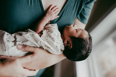 Newborn resting peacefully on mother’s chest in soft window light, swaddled in a dotted muslin wrap during a calm, baby-led session in Portland.