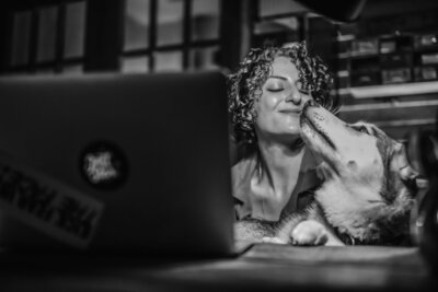 Hannah Ellaham - BYOBrand Podcast Host Smiling At Her Dog Yara The Husky while sitting in from of laptop