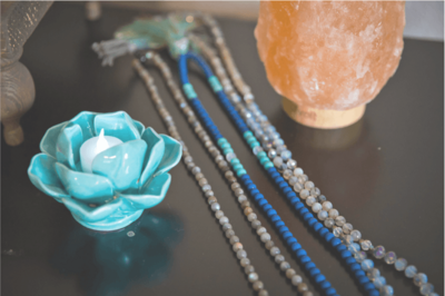Susan's yoga accessories sitting on a table top - includes a small blue lotus flower candle, prayer beads, and a salt lamp