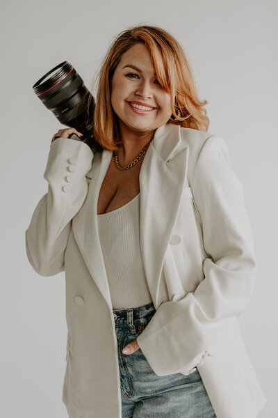 woman in a white suit smiling holding a camera
