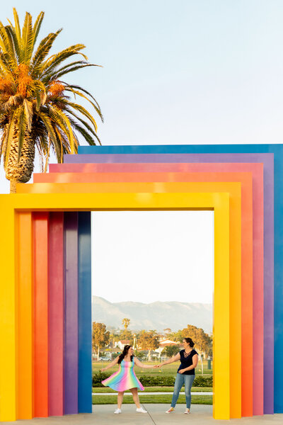 A couple dancing in the middle of a large, rainbow arch.