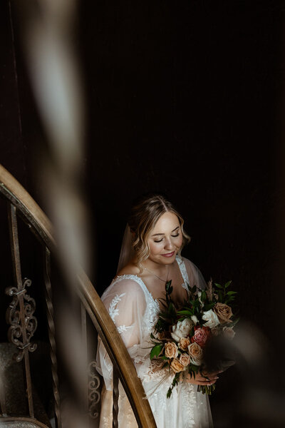 A bride looks down at her bouquet while going down the steps
