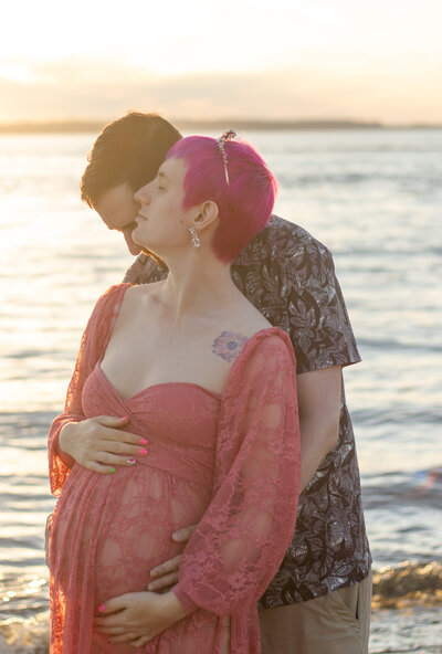 a couple with a pregnant person embrace as they dream about the future with a new baby at Edmond's Beach, Washington