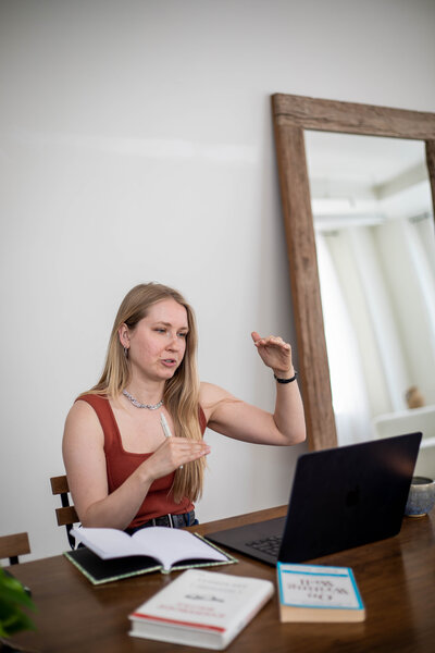 Krista Walsh (website copywriter) gesturing to explain her web copy process, with her laptop and notebook in front of her.