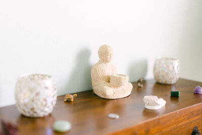A simple Buddha statue on a wooden shelf with candles and scattered gemstones, symbolizing tranquility and mindfulness.