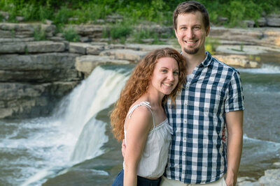 Smiling couple stands in front of waterfall