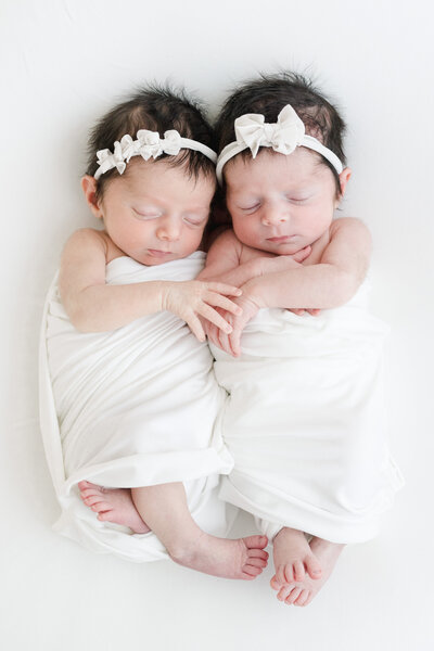 Sleeping newborn twin baby girls embrace during newborn photography session