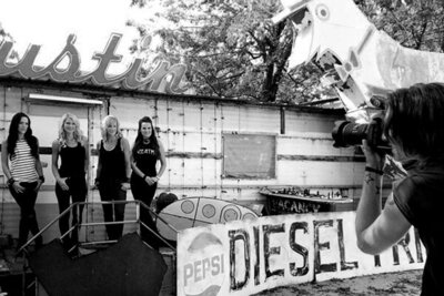 BTS photo band photography four members of female music group The Mrs standing against old building with Austin sign above it while Mark takes their photo black and white image