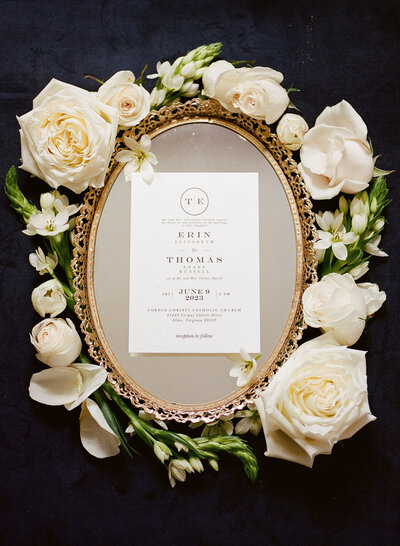 Wedding invite on a gold mirror surrounded by white florals by Northern Virginia wedding photographer Katie Annie