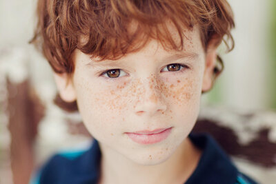 Close up portrait of a boy with brown eyes and tons of freckles looking directly into the camera.