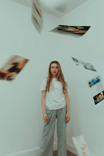 Creative branding photography session with a woman standing in a white room as printed images fall around her.